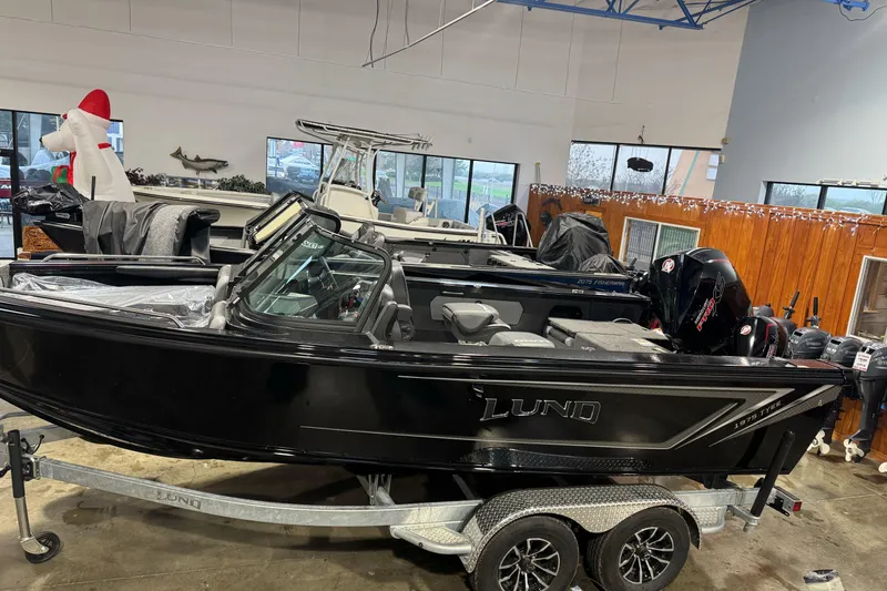 The Image of 2026 Lund 1975 Tyee boat in showroom, sleek black design on trailer. - 0