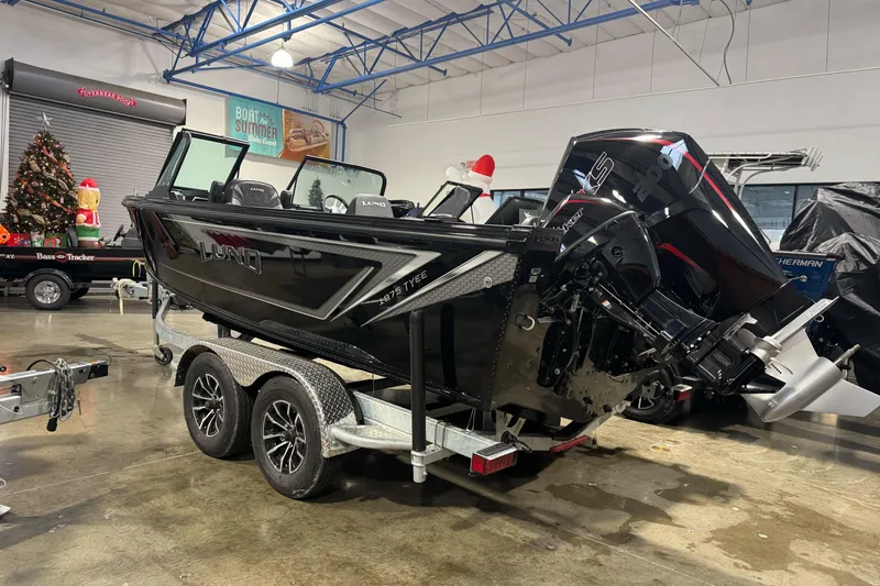 Slide: The Image of 2026 Lund 1975 Tyee boat on trailer in showroom, featuring sleek black design. - 6