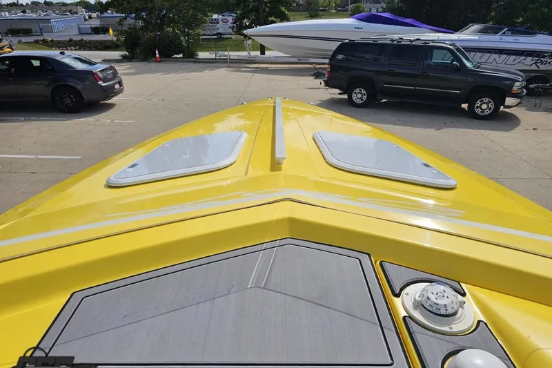 Slide: The Image of Yellow 2007 Baja 26 Outlaw boat parked, viewed from the bow, with cars in the background. - 73