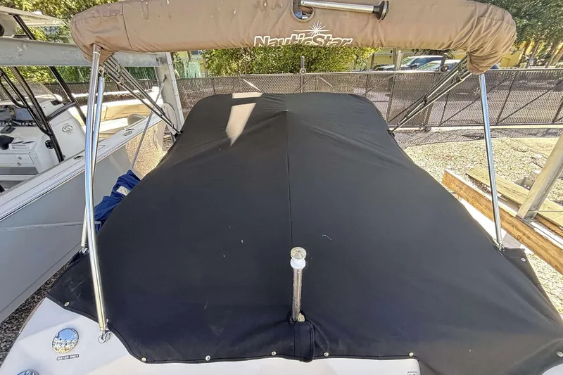 Slide: The Image of 2020 NauticStar 223 DC boat with black cover and bimini top in storage. - 5