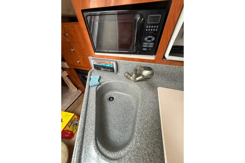 Slide: The Image of 2005 Larson Cabrio 290 boat kitchen with sink, microwave, and wooden cabinetry. - 39