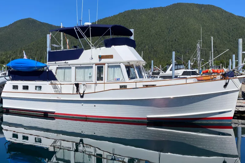 The Image of 1995 Grand Banks 42 Motoryacht docked, reflecting on calm water, with forested hills in the background. - 0