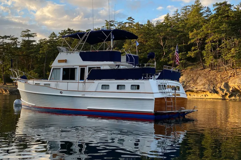 Slide: The Image of 1995 Grand Banks 42 Motoryacht anchored near a forested shoreline under a partly cloudy sky. - 3
