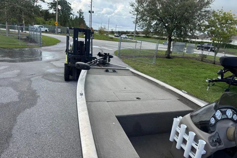 Slide: The Image of Forklift moving a 2020 Tracker boat on a wet pavement near a fenced area. - 8