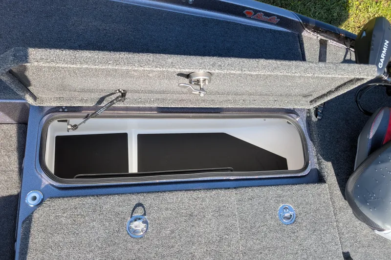 Slide: The Image of Open storage compartment in 2026 Bass Cat Eyra SP boat, featuring carpeted interior and Garmin equipment. - 18