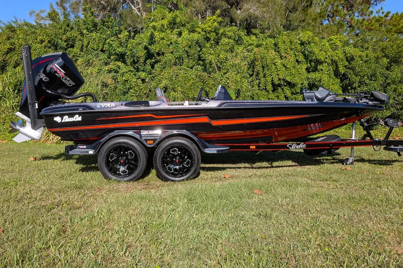 Slide: The Image of 2026 Bass Cat Eyra SP boat on trailer, black and red design, parked on grass. - 2