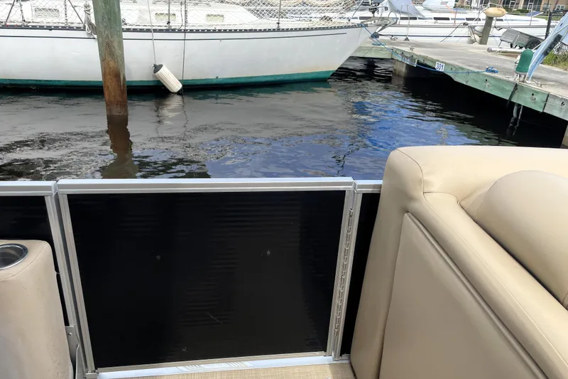 Slide: The Image of 2019 Harris Sunliner 250 pontoon boat interior at marina, with docked sailboat in background. - 11