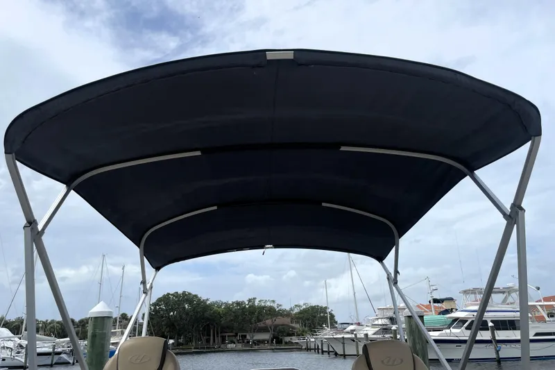 Slide: The Image of 2019 Harris Sunliner 250 boat with canopy, docked at marina under cloudy sky. - 26