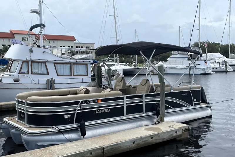 Slide: The Image of 2019 Harris Sunliner 250 pontoon boat docked at marina with other vessels. - 3