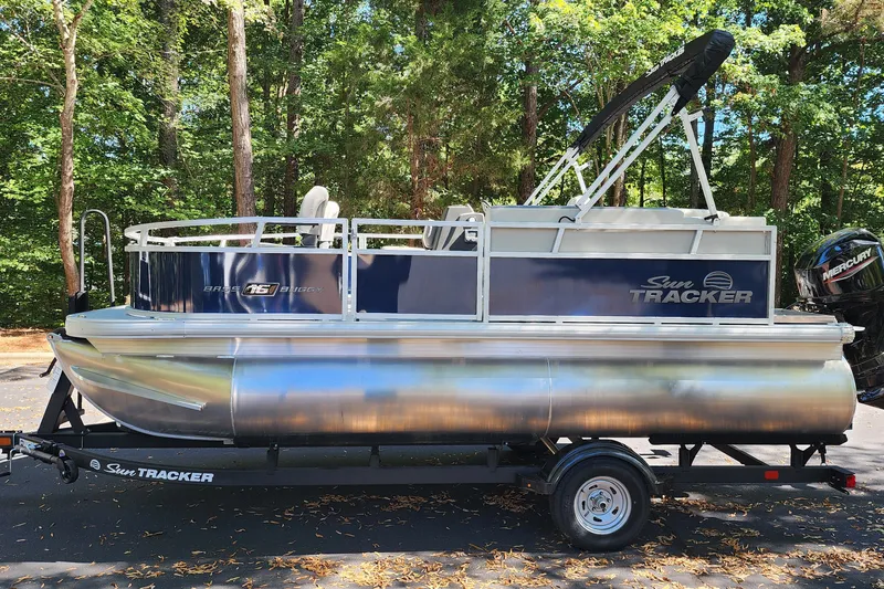The Image of 2026 Sun Tracker Bass Buggy 16 XL Select pontoon boat on trailer, surrounded by trees. - 0