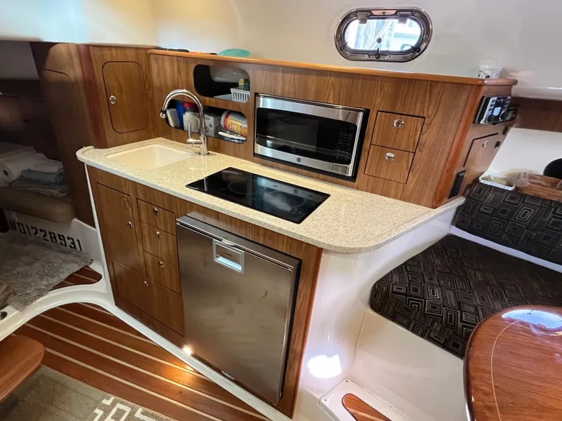 Slide: The Image of 2010 Pursuit OS 345 Offshore boat interior with kitchenette, featuring wood cabinetry and modern appliances. - 37