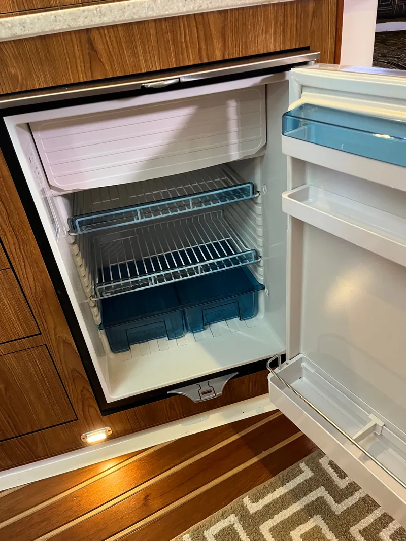 Slide: The Image of Open refrigerator inside 2010 Pursuit OS 345 Offshore boat, featuring wooden cabinetry and striped flooring. - 39