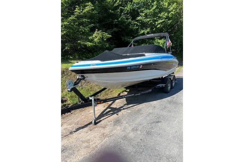 Slide: The Image of 2012 Crownline 215 SS boat on trailer, parked outdoors with trees in background. - 2