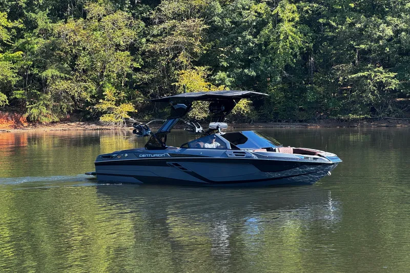 Slide: The Image of 2026 Centurion Ri230 boat cruising on a serene lake with lush forest backdrop. - 4