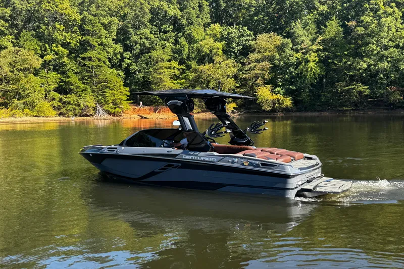 Slide: The Image of 2026 Centurion Ri230 boat cruising on a serene lake with lush green forest backdrop. - 6