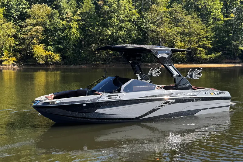 Slide: The Image of 2026 Centurion Ri230 boat on a calm lake with lush green trees. - 8