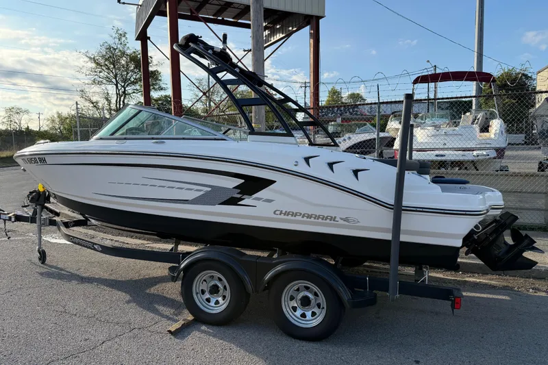 Slide: The Image of 2022 Chaparral 21 SSi boat on trailer, parked outdoors near a fence. - 2