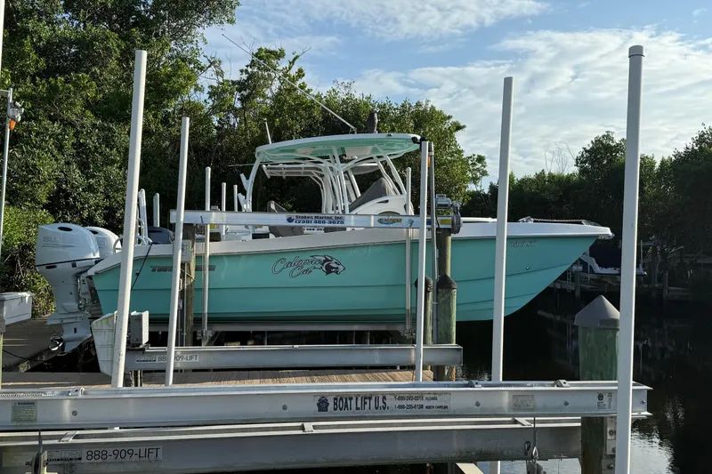 Slide: The Image of 2019 Twin Vee 26 Center Console boat on lift, surrounded by trees and water. - 14