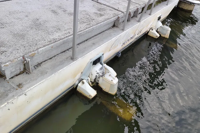 Slide: The Image of 1981 Lazy Days 50 houseboat docked, showing outboard motors and weathered deck. - 17