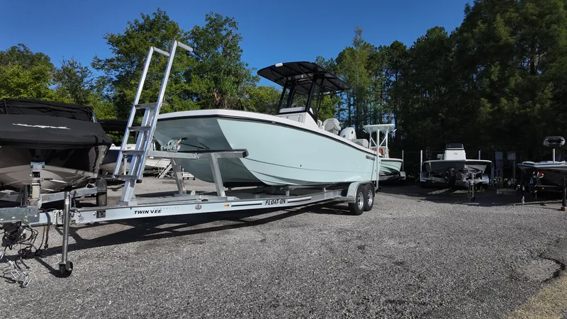 Slide: The Image of 2026 Twin Vee 22 Bay Cat boat on trailer, parked outdoors with trees in background. - 2