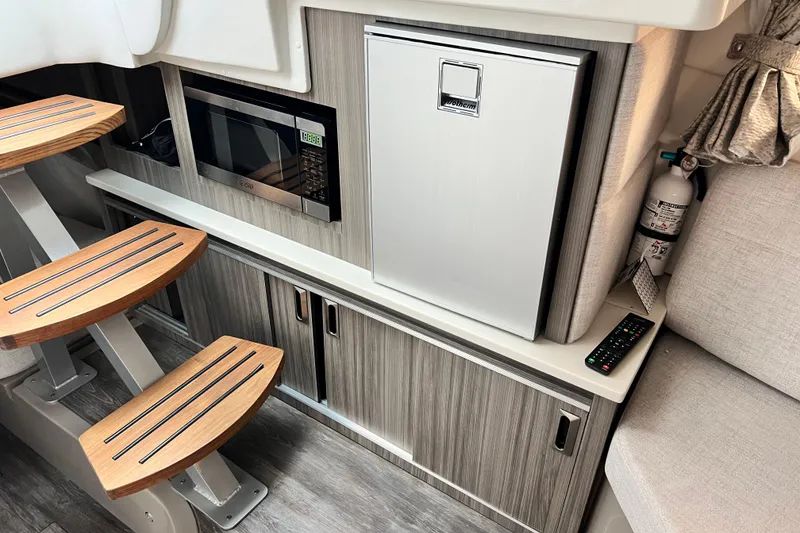 Slide: The Image of 2025 Sea Ray Sundancer 320 Outboard interior with microwave, fridge, and wooden steps. - 16