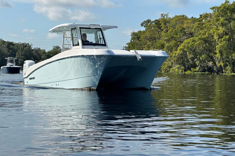 Slide: The Image of 2026 Twin Vee 280 GFX2 CC boat cruising on a calm river with lush greenery. - 2