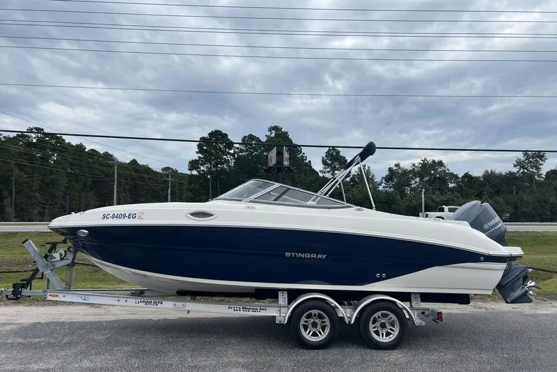 Slide: The Image of 2015 Stingray 234LR boat on trailer, parked outdoors under cloudy sky. - 0