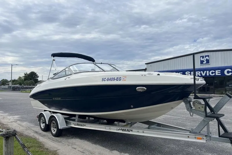 Slide: The Image of 2015 Stingray 234LR boat on trailer, parked near service center under cloudy sky. - 2