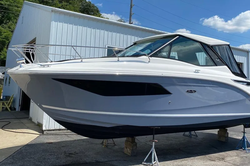 Slide: The Image of 2021 Sea Ray Sundancer 320 Coupe on stands, outside a white building under blue sky. - 2