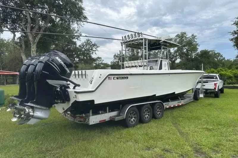 Slide: The Image of 2019 Contender 39 ST boat on trailer, triple Mercury engines, parked on grass. - 4