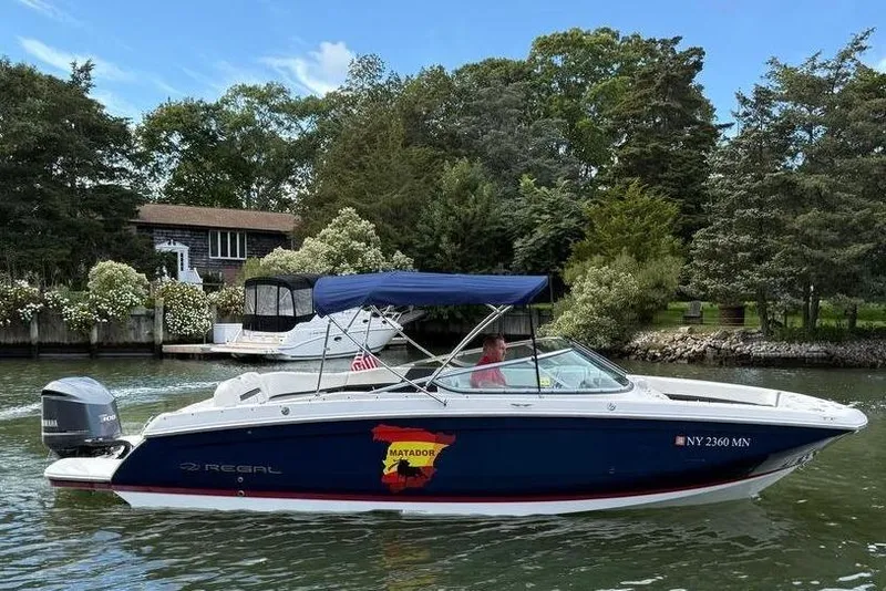 Slide: The Image of 2017 Regal 26 OBX boat on a calm river with lush greenery background. - 5