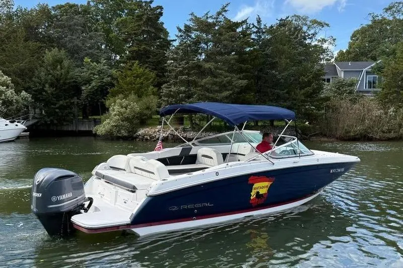 Slide: The Image of 2017 Regal 26 OBX boat cruising on a scenic waterway with lush greenery. - 6