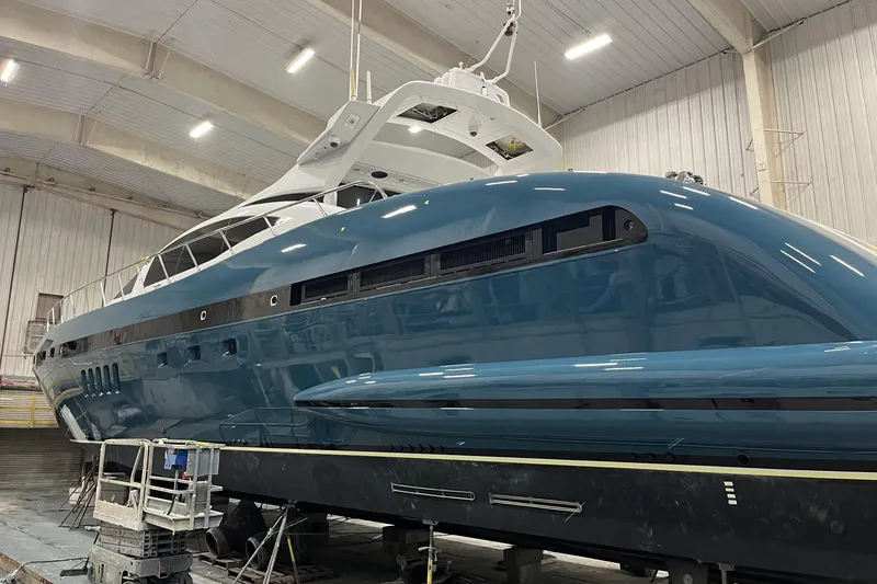 Slide: The Image of Mangusta 92 yacht from 2005 in a shipyard, showcasing sleek design and blue hull. - 3