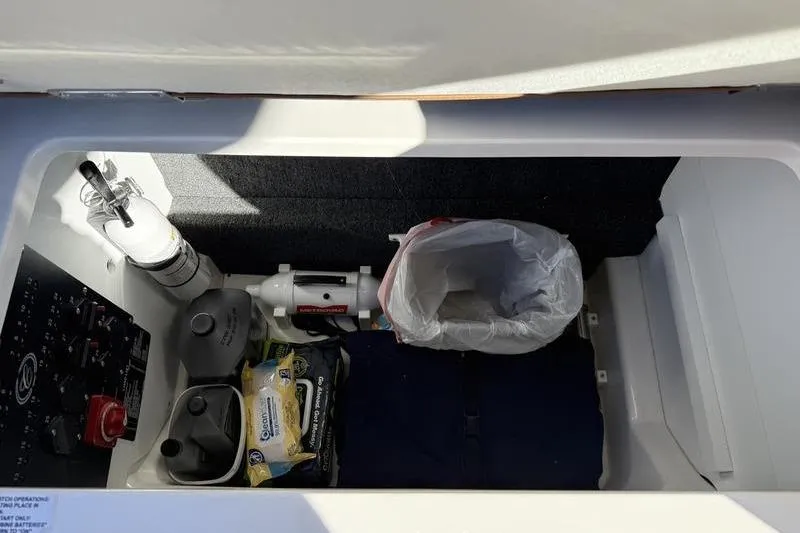 Slide: The Image of Storage compartment in a 2022 Cobalt R6 boat, featuring safety equipment and cleaning supplies. - 16