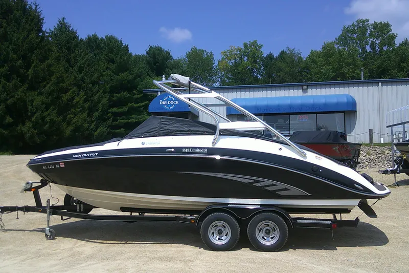 Slide: The Image of 2010 Yamaha Boats 242 Limited S on trailer, parked outdoors near trees and building. - 30