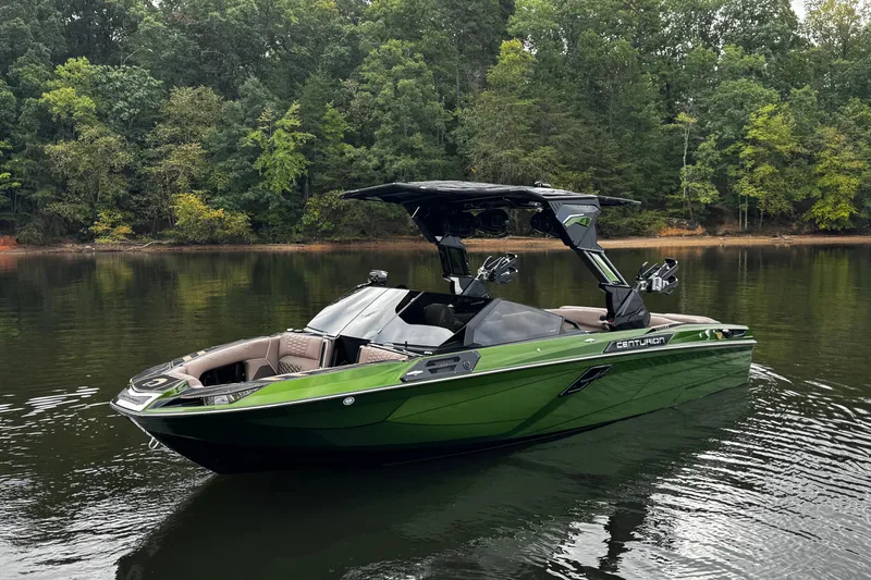 Slide: The Image of 2026 Centurion Ri245 boat in green, floating on a calm lake with forested background. - 2