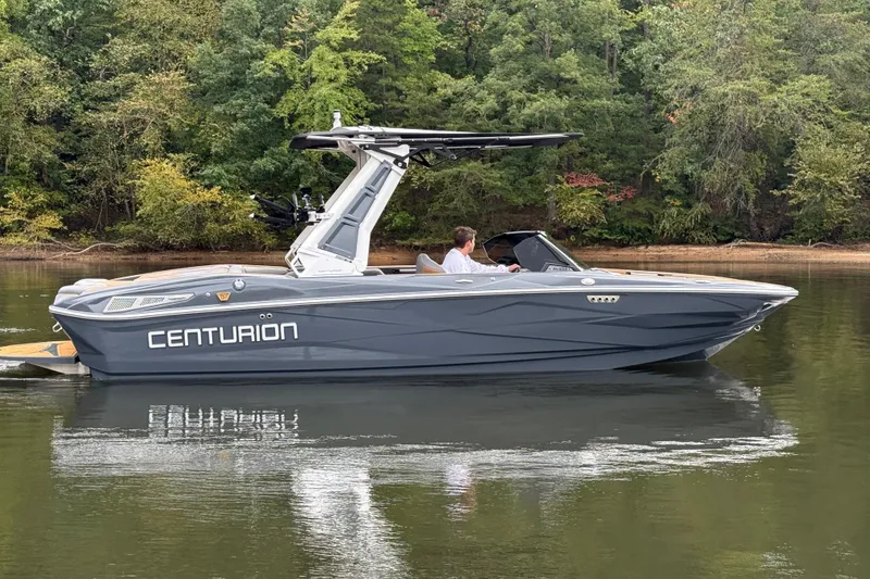 Slide: The Image of 2026 Centurion Nv233 boat on calm lake with lush green forest backdrop. - 13