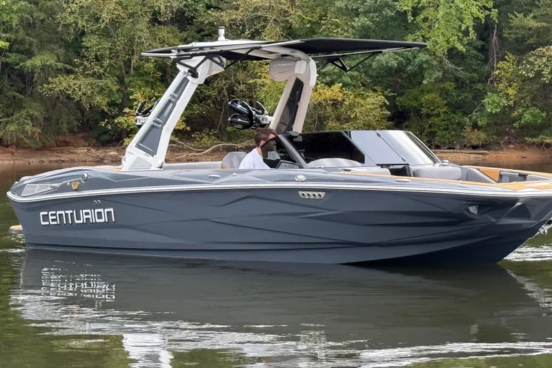 Slide: The Image of 2026 Centurion Nv233 boat on calm water, surrounded by lush greenery. - 7