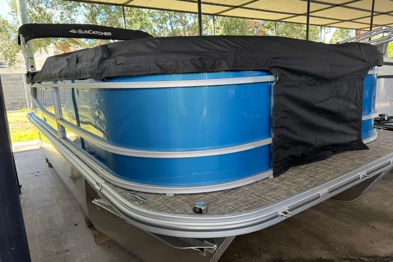 Slide: The Image of 2026 SunCatcher Select 22RC pontoon boat with blue exterior and black cover in a sheltered area. - 2