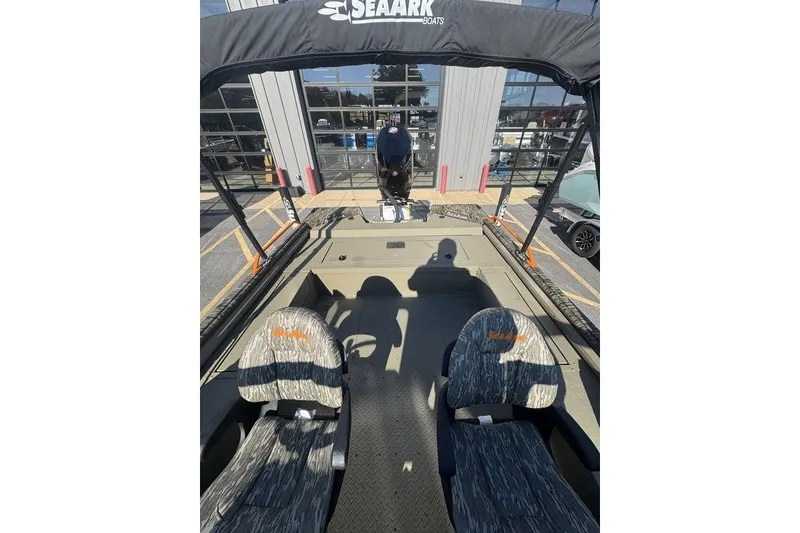 Slide: The Image of 2026 SeaArk EasyCat boat interior with camo seats and canopy, parked outside a building. - 23