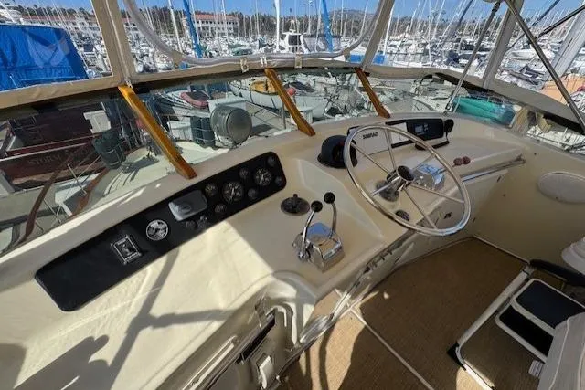 Slide: The Image of 1985 Tollycraft 48 Cockpit Motor Yacht helm with marina view, showcasing controls and steering wheel. - 10