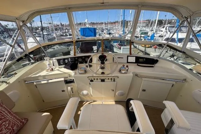 Slide: The Image of 1985 Tollycraft 48 Cockpit Motor Yacht helm with marina view, featuring steering wheel and controls. - 9