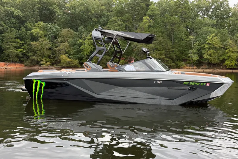 Slide: The Image of 2021 Nautique Super Air Nautique G23 boat on a calm lake with forest backdrop. - 7