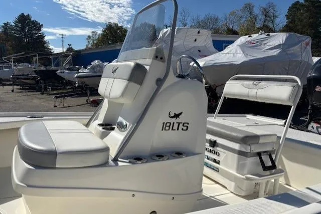 Slide: The Image of 2024 Mako 18 LTS boat interior with seating and console, parked outdoors. - 14