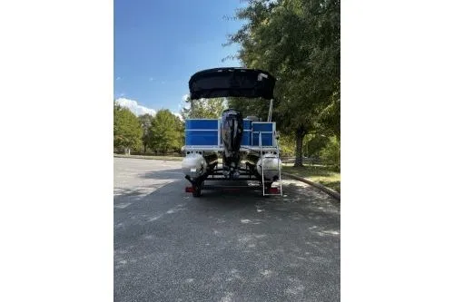 Slide: The Image of 2026 Sun Tracker Party Barge 18 DLX pontoon boat parked, rear view, under trees. - 3