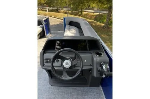 Slide: The Image of 2026 Sun Tracker Party Barge 18 DLX steering console with seating, surrounded by trees. - 5