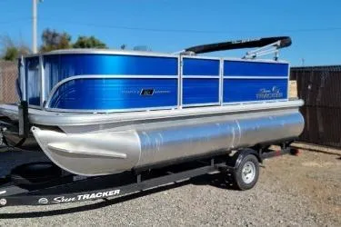 Slide: The Image of 2026 Sun Tracker Party Barge 16 DLX pontoon boat on trailer, blue and silver design. - 2