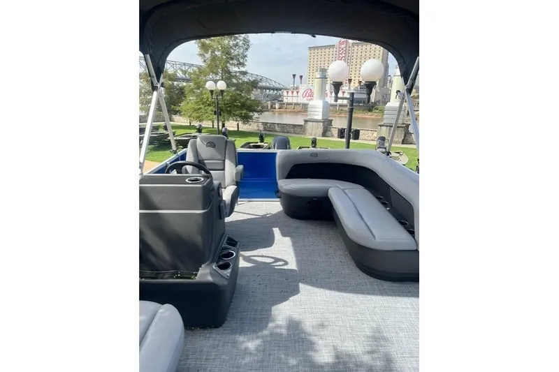 Slide: The Image of 2026 Sun Tracker Party Barge 16 DLX interior with seating and helm, docked by a scenic river. - 4