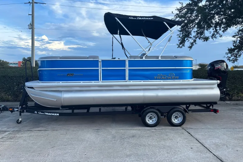 The Image of 2026 Sun Tracker Party Barge 20 DLX pontoon boat on trailer, blue and silver design. - 0