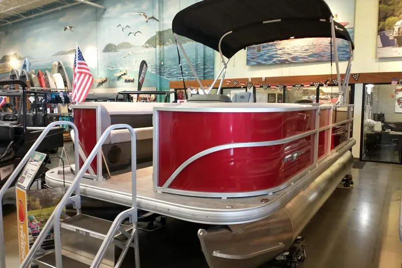 The Image of 2026 Sun Tracker Party Barge 18 DLX pontoon boat displayed indoors with American flag. - 0